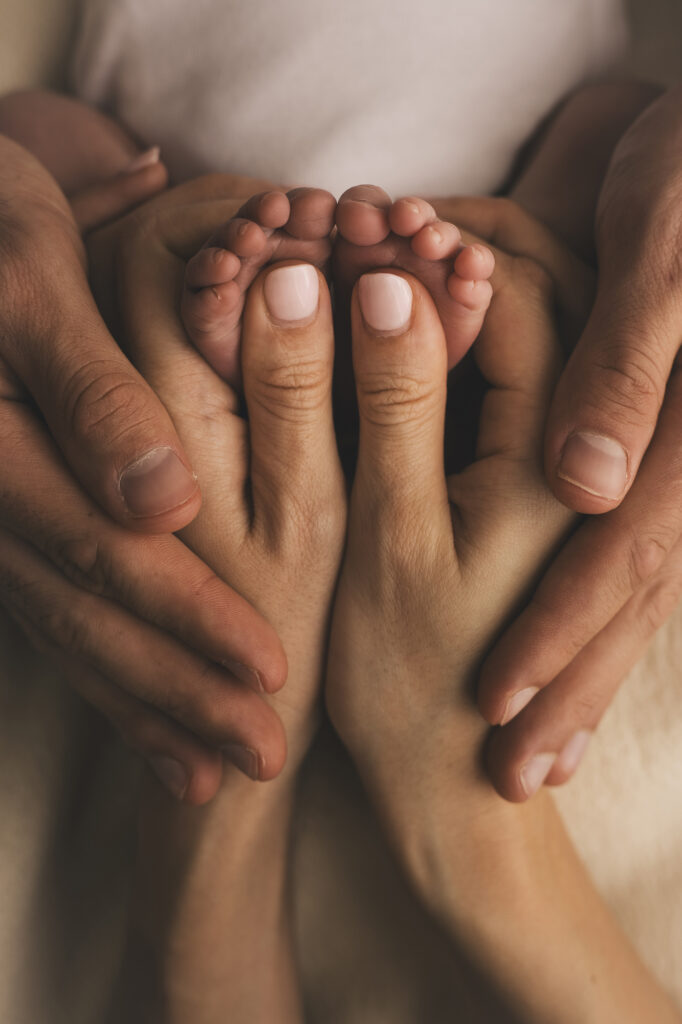 Mãos dos pais a envolver os pés minúsculos do bebé recém-nascido, captando um momento de união familiar.